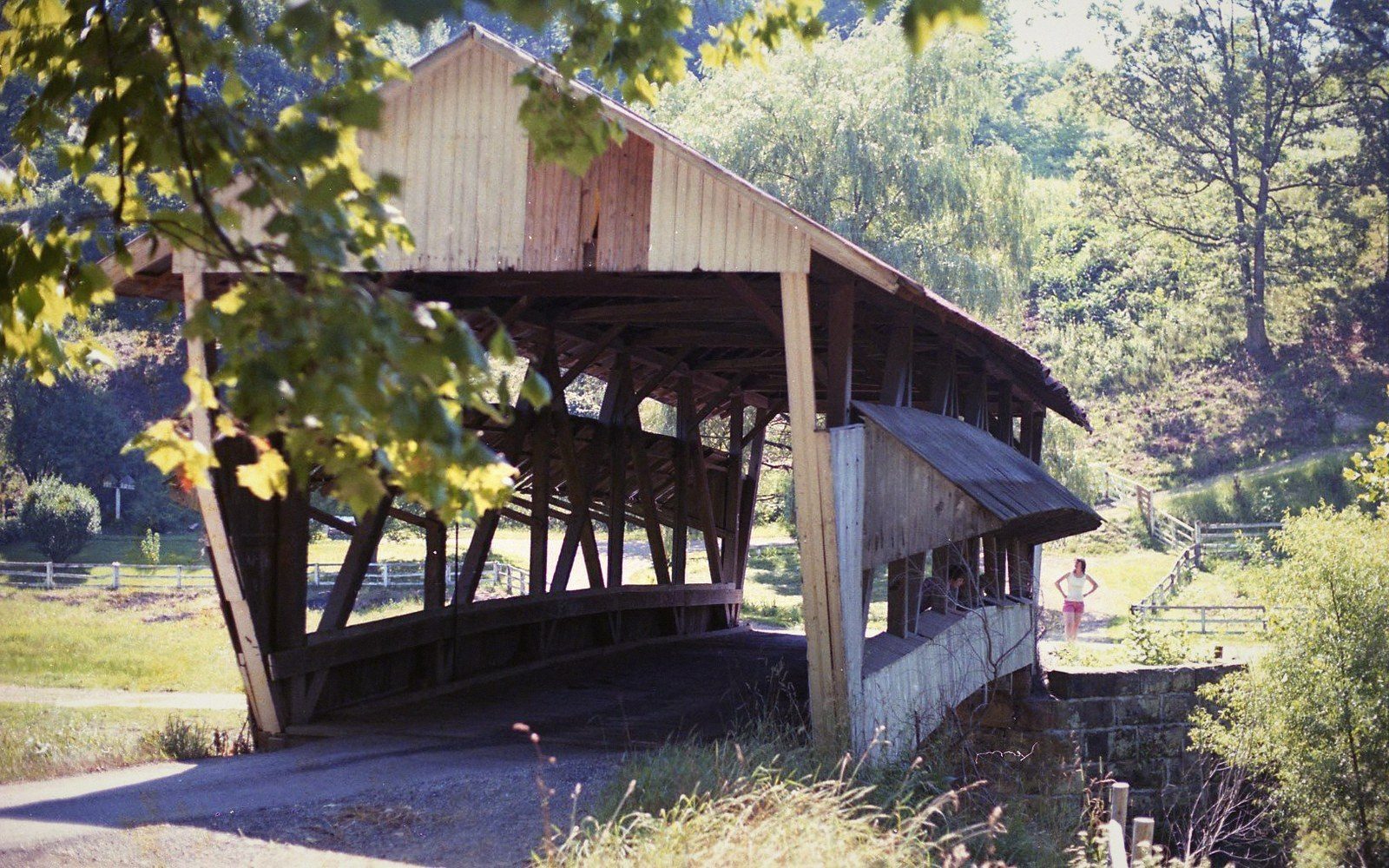 Wooden covered bridge with exposed truss framework spans a road amid trees