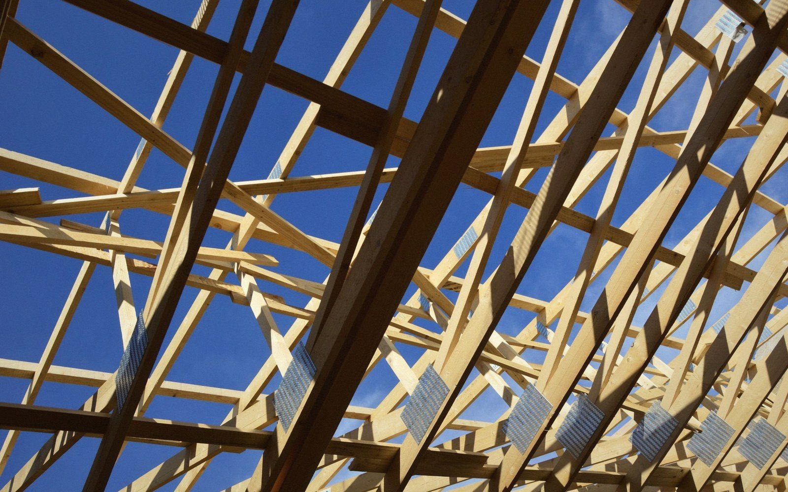 Wooden roof trusses with metal connector plates seen from below against blue sky