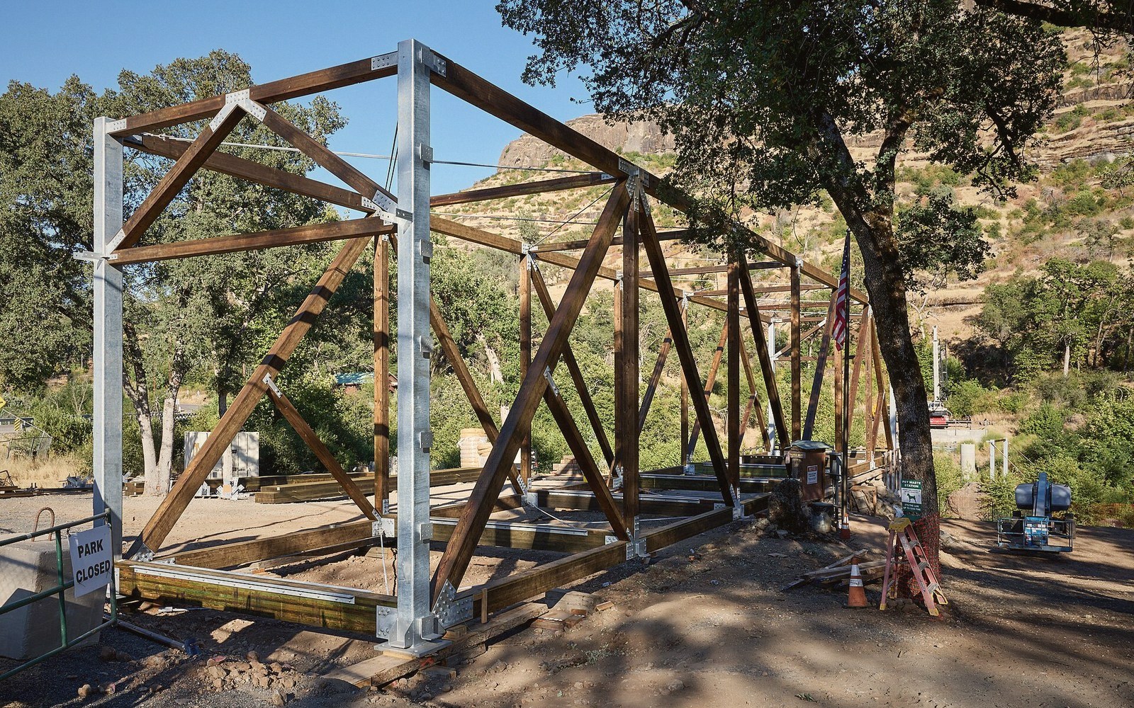 Wooden truss framework under construction for a covered bridge, with hills in the background