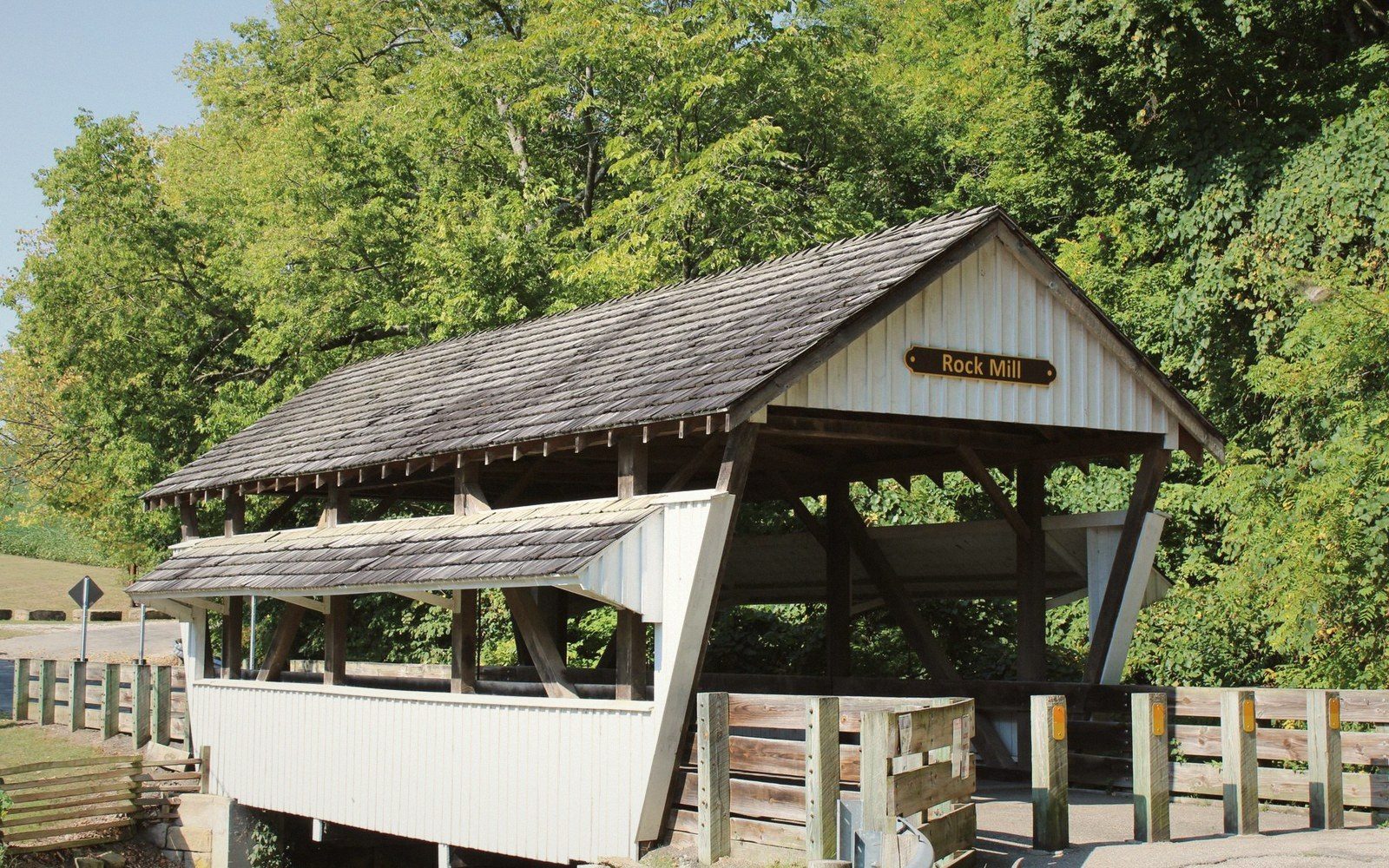 Wooden covered bridge labeled Rock Mill surrounded by dense green trees