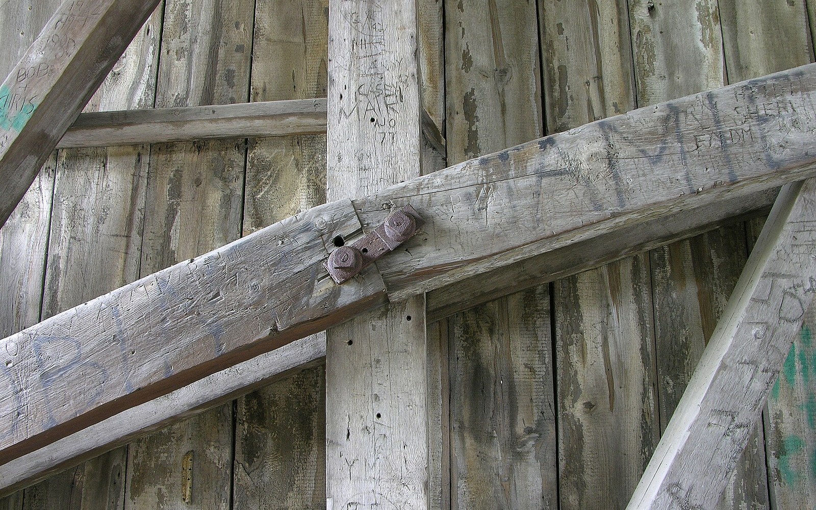 Weathered wooden beams joined with rusty bolts, covered in carved graffiti