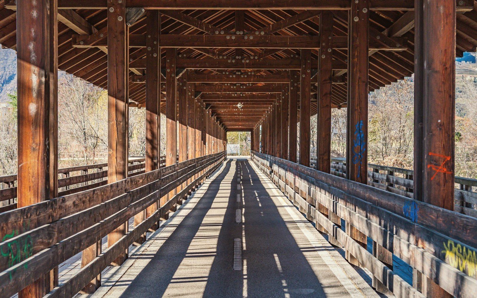 Wooden covered bridge with rows of timber beams casting long shadows on the walkway