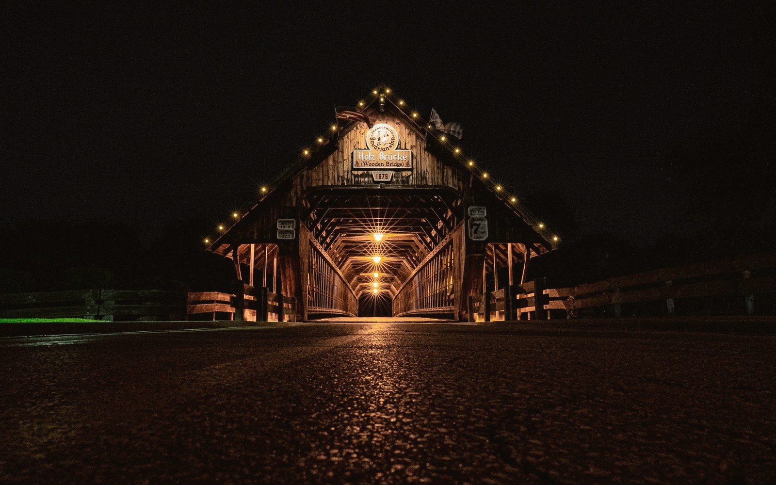 A covered wooden bridge lit with string lights glowing against a dark night sky