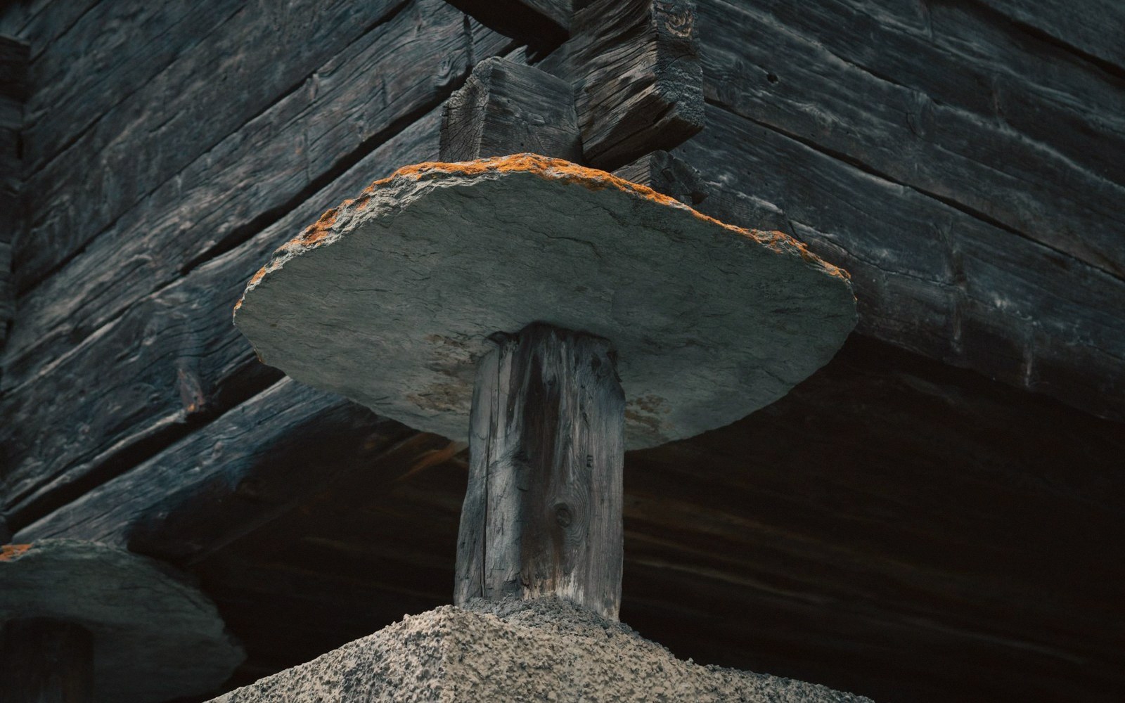 A flat stone slab rests on a wooden post supporting a timber granary building