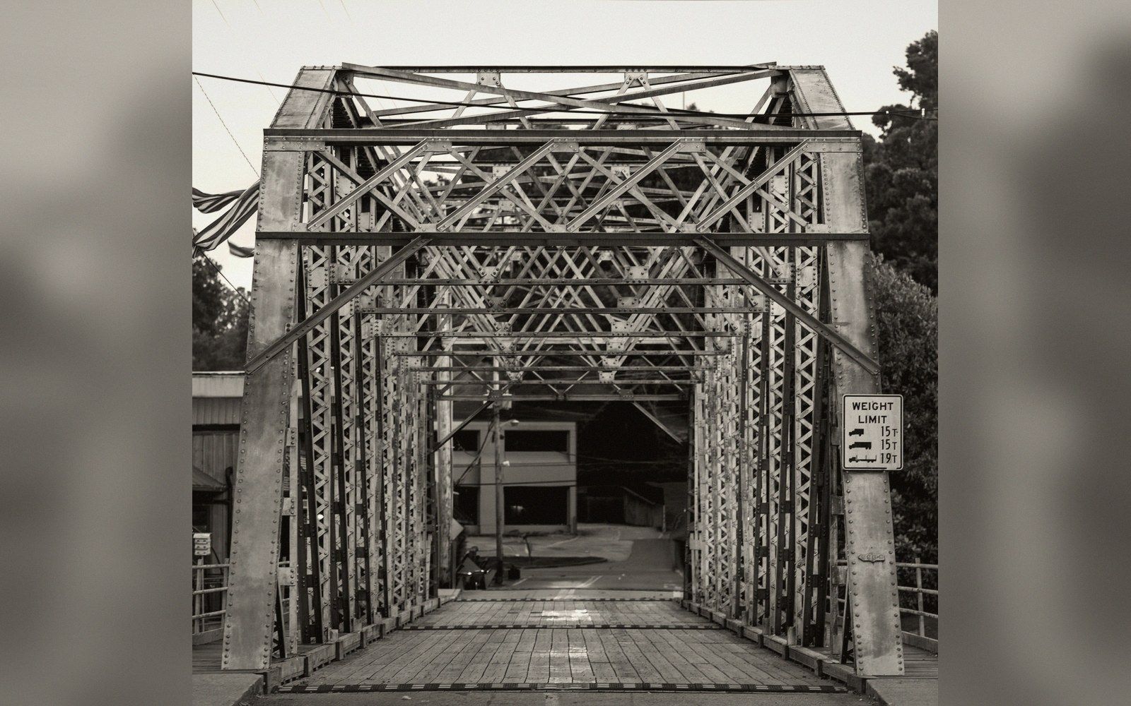 Steel truss bridge entrance with a weight limit sign posted at the side