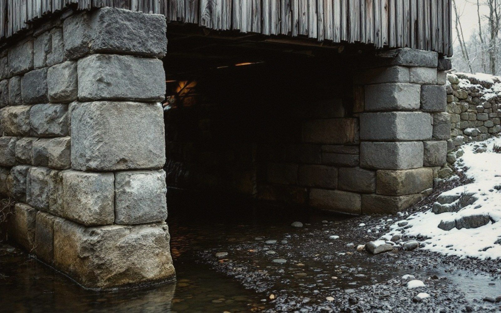 A coursed stone abutment where a bridge meets the bank, the creek low beneath it